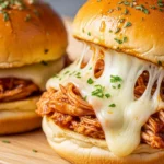 A rustic wooden tray filled with cheesy BBQ pulled chicken sliders featuring a garlic butter glaze on sweet Hawaiian rolls.