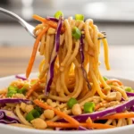An individual serving of cold pasta salad with peanut sauce being lifted with a fork, perfect for budget-friendly meal prep.