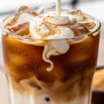 A tall glass showing the beautiful cascading layers of a refreshing Iced Brown Sugar Oatmilk Shaken Espresso, featuring thick, frothy coffee and creamy milk over ice.