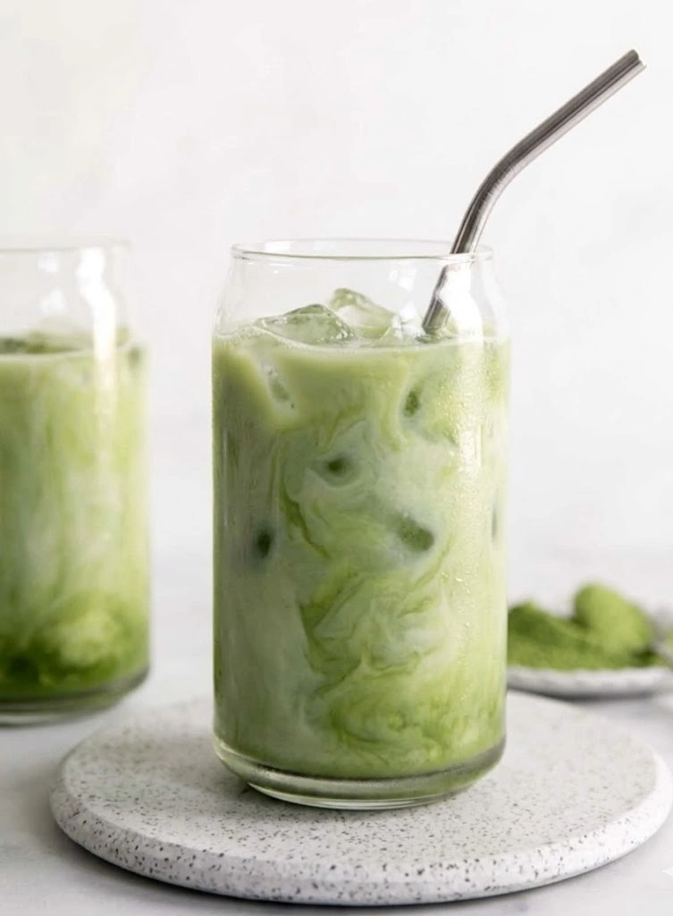 A tall glass filled with a refreshing iced matcha latte, featuring beautiful swirls of bright green matcha and creamy oat milk over ice with a bamboo straw.