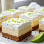 A perfect square slice of Key Lime Pie Bars topped with a dollop of whipped cream, fresh lime zest, and a lime slice on a white dessert plate.