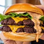 A candid, naturally lit photo of a person holding a juicy, crispy smash burger with house sauce, melted American cheese, and fresh lettuce on a toasted brioche bun.