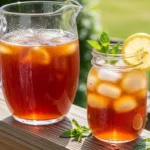 A candid, natural photo of a cold, condensation-covered mason jar filled with a classic Southern Sweet Tea Recipe over ice, garnished with fresh lemon and mint on a sunlit front porch.