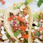 Three authentic cilantro lime chicken tacos in a rustic holder, loaded with grilled chicken, avocado, red onion, and cotija cheese for an easy weeknight dinner.