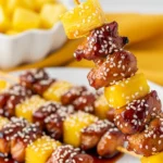 A white plate of sticky air fryer teriyaki chicken kabobs with charred pineapple and bell peppers, garnished with sesame seeds and green onions.