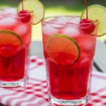 A close-up, refreshing shot of a Sonic copycat cherry limeade in a tall glass covered in condensation, garnished with a bright green lime wheel and a sweet red cherry.