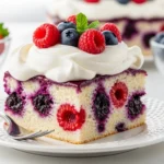 A perfectly sliced square of Summer Berry Poke Cake on a white plate, revealing a beautiful red white and blue dessert with vibrant berry sauce stripes hidden inside the moist cake.