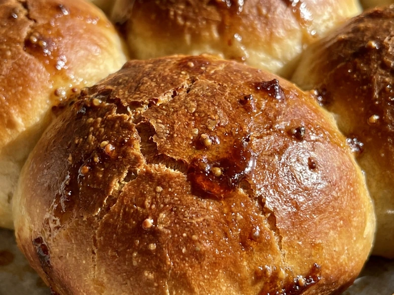 A stunning macro close-up of a freshly baked Crack Breakfast Slider, focusing on the dimpled, deeply golden-brown Hawaiian roll top that is beautifully caramelized with a sticky, mouth-watering maple butter glaze.