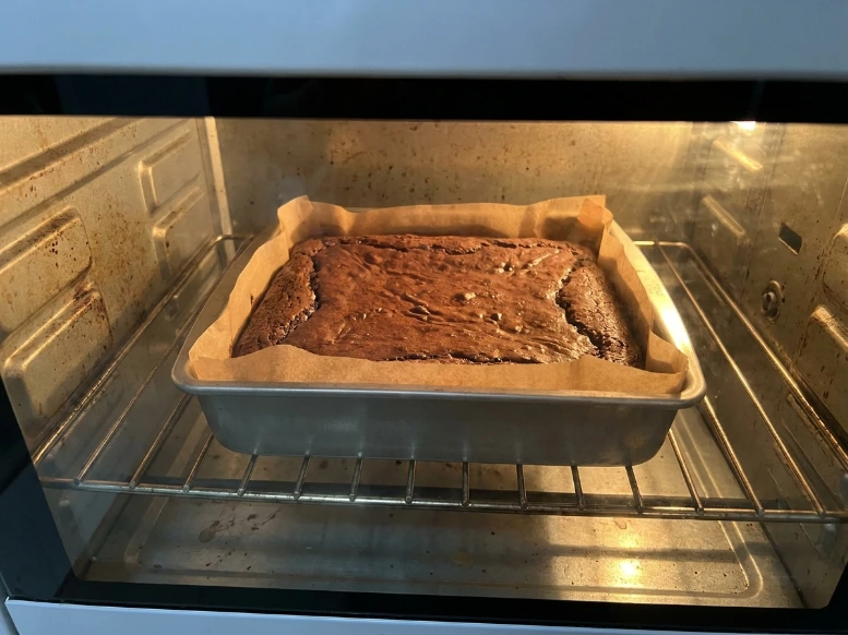A square metal pan of chocolate zucchini brownies baking inside a hot oven on the middle wire rack until the edges are firmly set.